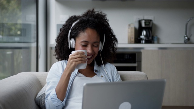 漂亮的黑人女人在家里用笔记本电脑看电影戴着耳机享受着热巧克力视频下载