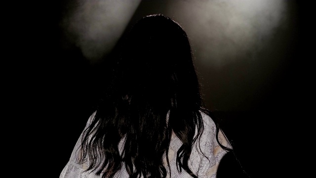 一个女人在白色聚光灯下的黑暗舞台上的肖像。视频下载