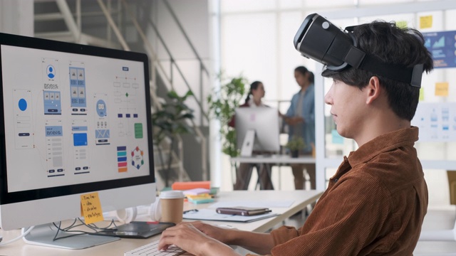年轻的亚洲设计师编码和戴vr眼镜(虚拟现实)测试移动应用程序，从桌面电脑开发软件在现代创意办公室视频素材