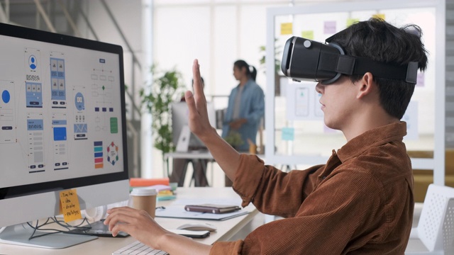 年轻的亚洲设计师使用虚拟现实眼镜(虚拟现实)测试手机应用程序开发与桌面电脑在现代创意办公室视频素材