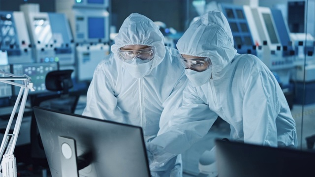 研究工厂洁净室:穿着工作服的工程师和科学家在计算机上交谈和工作，用显微镜检查主板微处理器，为医疗电子开发电子视频素材