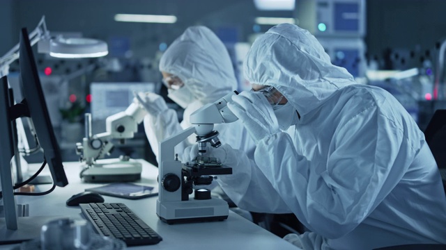 研究工厂洁净室:工程师/科学家穿着工作服和手套使用显微镜检查主板微处理器组件，开发高科技现代电子视频素材