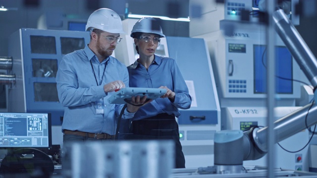 工厂车间:专业女工程师，男机械操作员，用工业平板电脑工作，为生产线机械手编程。高科技设备与数控机床视频素材