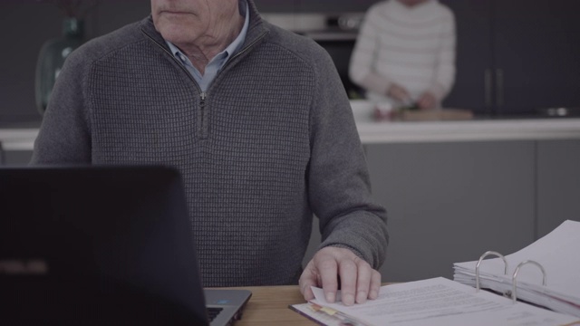 年长的成年男性在厨房桌子上用笔记本电脑做家庭财务，生活中的一天视频素材