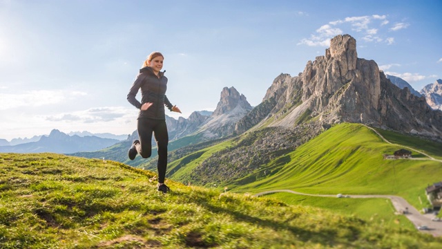 年轻的女运动员在山区的草地上跑步视频下载