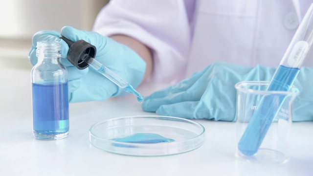 科学家或医务人员穿着实验服在实验室进行研究，在临床实验室的玻璃设备上混合滴入彩色液体试剂的4K视频片段视频素材