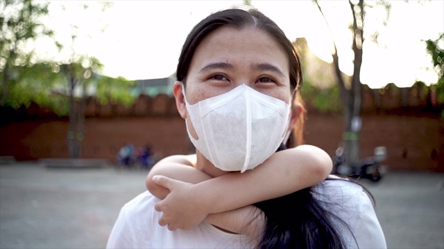 SLO MO垃圾女孩骑在妈妈的背上，她的妈妈戴着医用口罩在公园散步，以保护细菌视频购买
