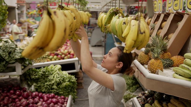 拉丁美洲妇女在水果和蔬菜摊上工作，挂着香蕉视频素材