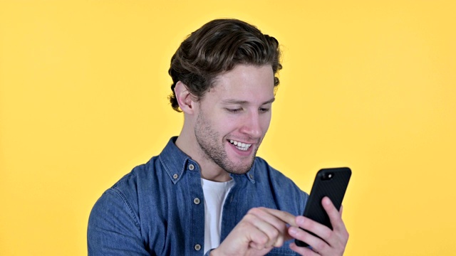 年轻人在智能手机上庆祝，黄色背景下的成功视频素材