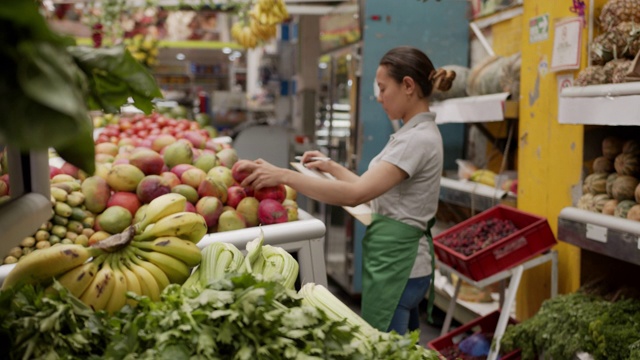 拉丁美洲的女售货员正在她的市场摊位上用写字板清点蔬菜视频下载