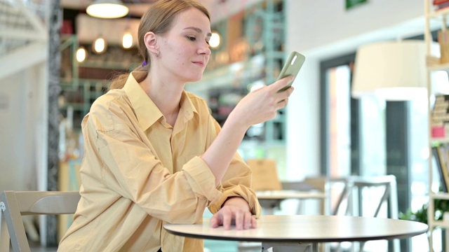 一名年轻女子在咖啡馆用智能手机刷屏视频素材