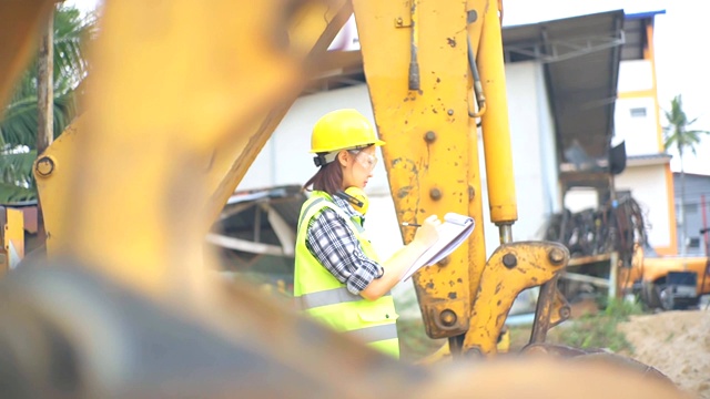 亚洲女工程师站在挖掘机的长柄勺旁，检查一个方案视频素材