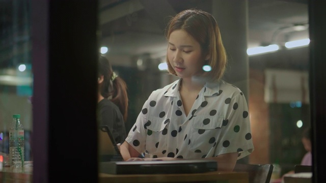年轻的商业女性在笔记本电脑上查东西，晚上在咖啡店里使用文件视频素材
