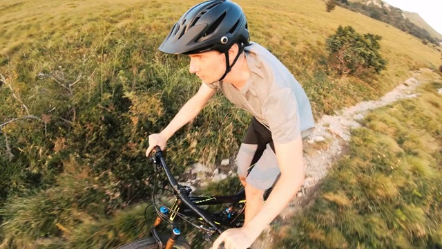 在一个阳光明媚的日子里，一名男子在绿草如茵的高山上骑行视频素材