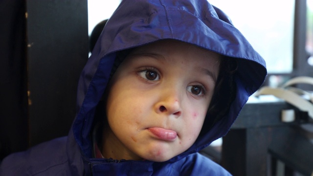 穿着蓝色雨衣的小男孩。孩子在雨天向外看的肖像视频下载