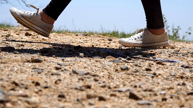 女性徒步旅行者的脚在山顶的悬崖。穿着运动鞋的女孩的双腿踩在岩石上。女游客在山上的小路上徒步旅行。夏季冒险的概念。低的观点视频素材