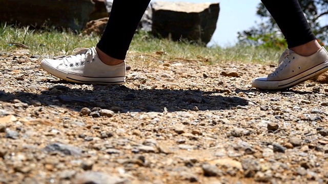 女性徒步旅行者的脚在山顶的悬崖。穿着运动鞋的女孩的双腿踩在岩石上。女游客在山上的小路上徒步旅行。夏季冒险的概念。低的观点视频素材