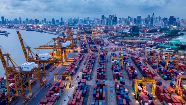 鸟瞰曼谷泰国工业进出口港口，集装箱成排成排，大型集装箱装载机船在夜间航行。视频下载