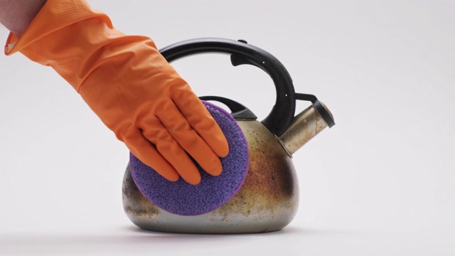 在白色背景下，手持橙色橡胶手套清洗金属水壶。做家务视频下载