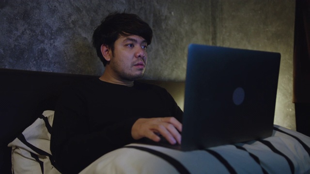 一个年轻人坐在卧室里用笔记本电脑视频素材