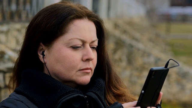 一个女人戴着耳机，手里拿着智能手机的肖像在秋天的街道上视频素材