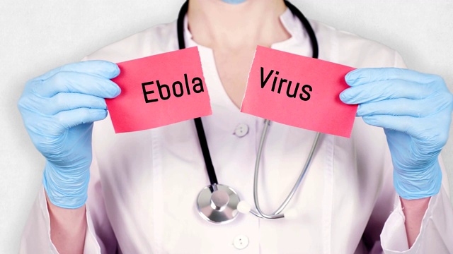 特写镜头，手在蓝色医疗手套握和撕破红色纸卡上的题字埃博拉病毒。医生穿着白色医疗制服，有听诊器视频下载