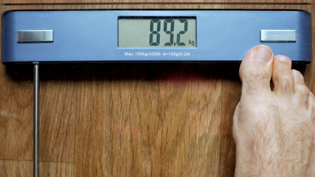 一个严重超重的人用电子秤称自己的体重。男人光着脚站在体重秤上。糖尿病饮食过量。视频下载