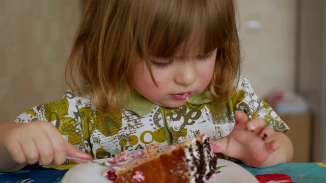 可爱的小男孩吃着新鲜甜蜜的巧克力蛋糕。特写镜头。迷人的小男孩，大大的眼睛里充满了爱和鲜奶油，用手指舔奶油，然后用涂满奶油的手指坐在桌前吃视频素材