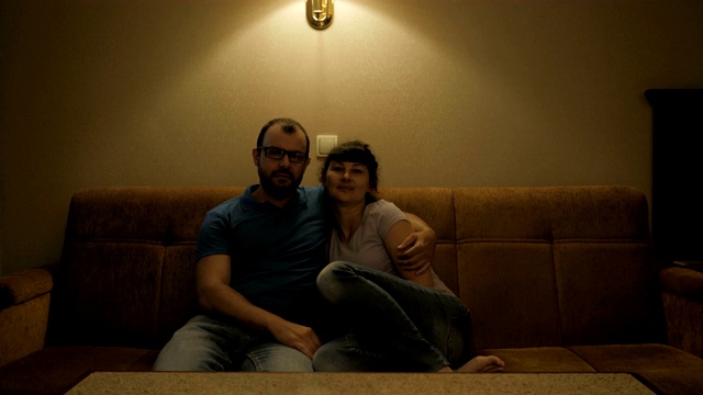 夫妻俩在电视上看电影。一对轻松的夫妇躺在舒适的客厅的沙发上看电视。一对恋人在客厅的沙发上拥抱着看电视。视频下载