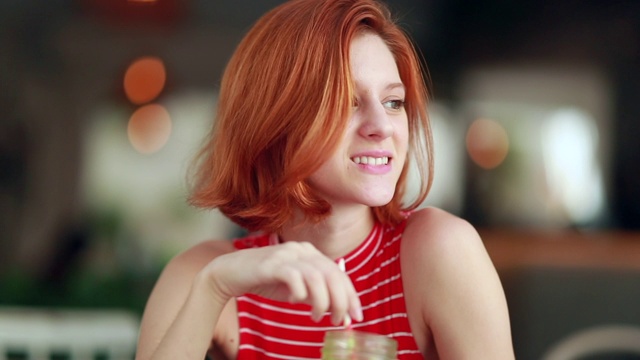 沉思美丽的红发女孩拿着绿色的果汁搅拌稻草视频素材