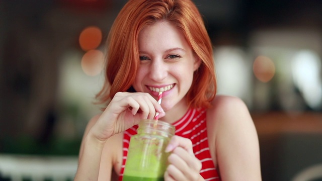 漂亮女孩喝绿色果汁。漂亮的红发年轻女子拿着健康的饮料视频素材