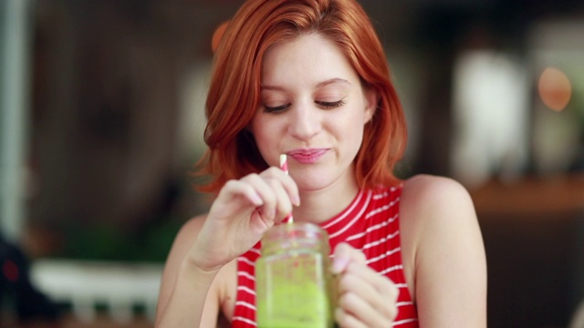 女孩喝着绿色的果汁，漂亮的红发年轻女子捧着健康的饮料视频素材