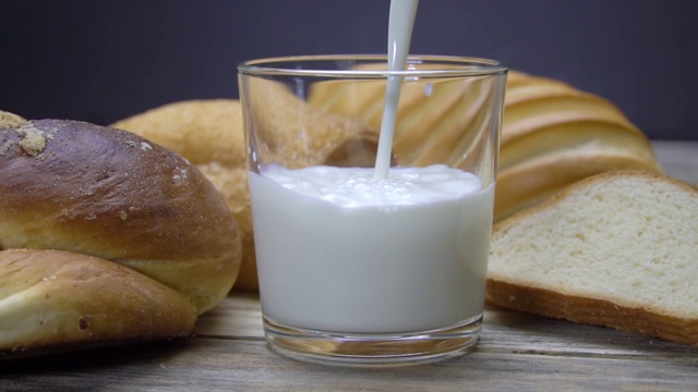 乡村厨房里的早餐，面包和牛奶。慢动作将牛奶倒入杯中。视频下载