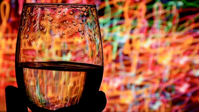 在模糊的黑色背景上，金色的白葡萄酒在玻璃杯中摇摆。葡萄酒广告的美丽库存镜头。品酒师在玻璃杯中调酒，在品酒时评价颜色。慢动作拍摄视频下载