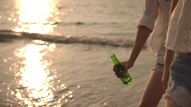 慢动作的手在日落的海滩上敬啤酒瓶，胜利，庆祝视频下载