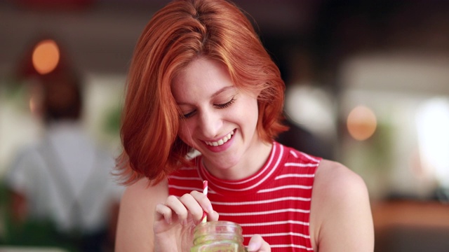 快乐漂亮的红头发喝健康的绿色果汁。年轻的红发女人拿着天然的排毒饮料视频素材