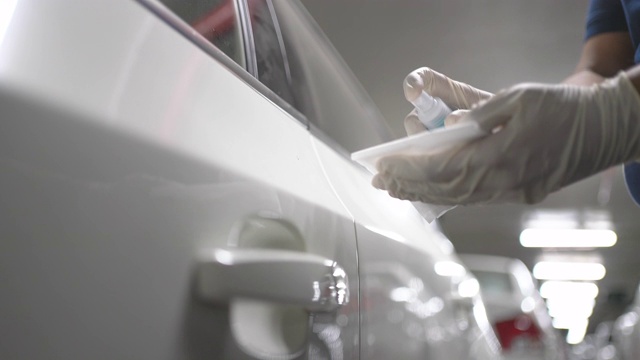在公寓停车场，手戴手套擦拭清洁新冠病毒的白色汽车门把手表面视频下载