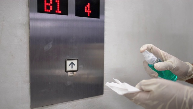 一名男子戴着塑料手套在公寓的电梯按钮上喷洒酒精视频下载