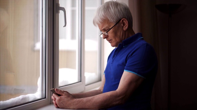 帅气的男人穿着蓝色polo t恤在家里用智能手机。视频下载