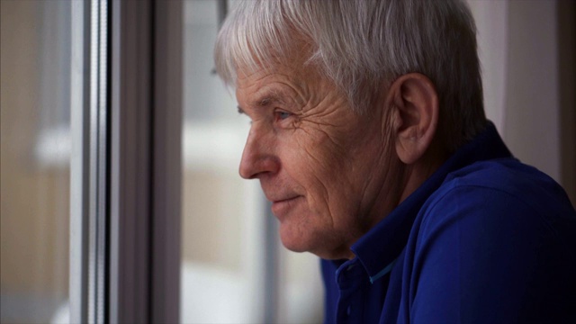 一个积极的退休男子在家站在窗户附近看窗户。视频素材