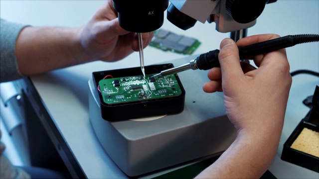 专业技术人员用烙铁修理显微镜台上的无人机组件。视频下载
