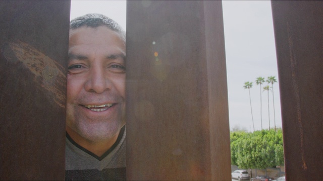一名西班牙裔男子在他的四十多岁偷窥墨西哥和美国之间的钢条边境墙，同时微笑和大笑的摄像机从美国一侧拍摄他的慢动作镜头视频下载
