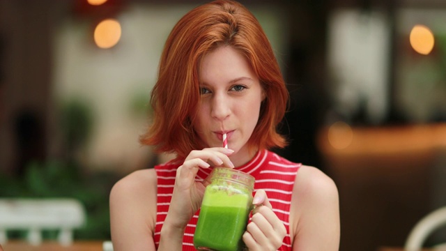 快乐的红发女孩喝着排毒绿汁笑着视频素材