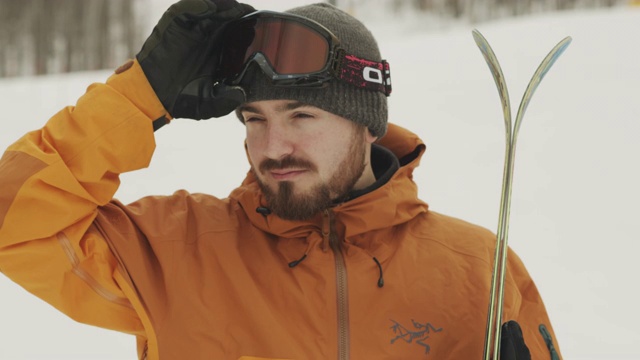 微笑的男性滑雪者一边拿着滑雪板一边调整他的眼镜。股票视频视频素材