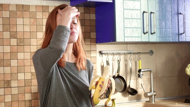 迷人的饥饿红发女孩在周末的清晨在厨房吃了一个大香蕉。清洁皮。健康饮食，正确的生活方式。体育的早餐。视频素材