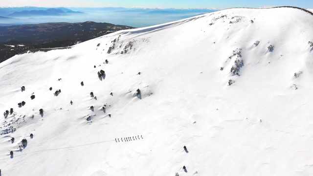 冬季高山登山队在高海拔山峰上排成一行行走的镜头视频下载