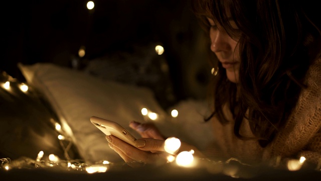 女人在圣诞节装饰的房间里躺在床上拿着电话。视频下载