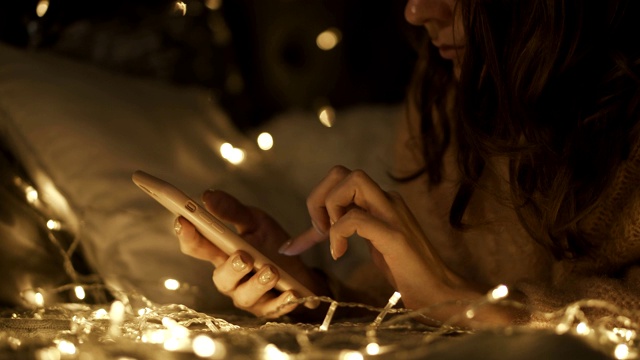 女人躺在圣诞装饰的房间的床上，用电话聊天视频下载