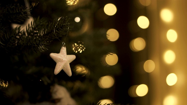 圣诞树上挂着圣诞小星星玩具和圣诞彩灯。装饰圣诞树。背景中花环的温暖散焦。视频下载