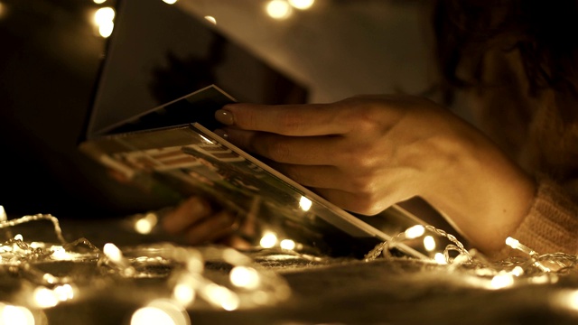被圣诞彩灯包围的女人用拇指指着一本旧相册。圣诞假期。锅了视频下载